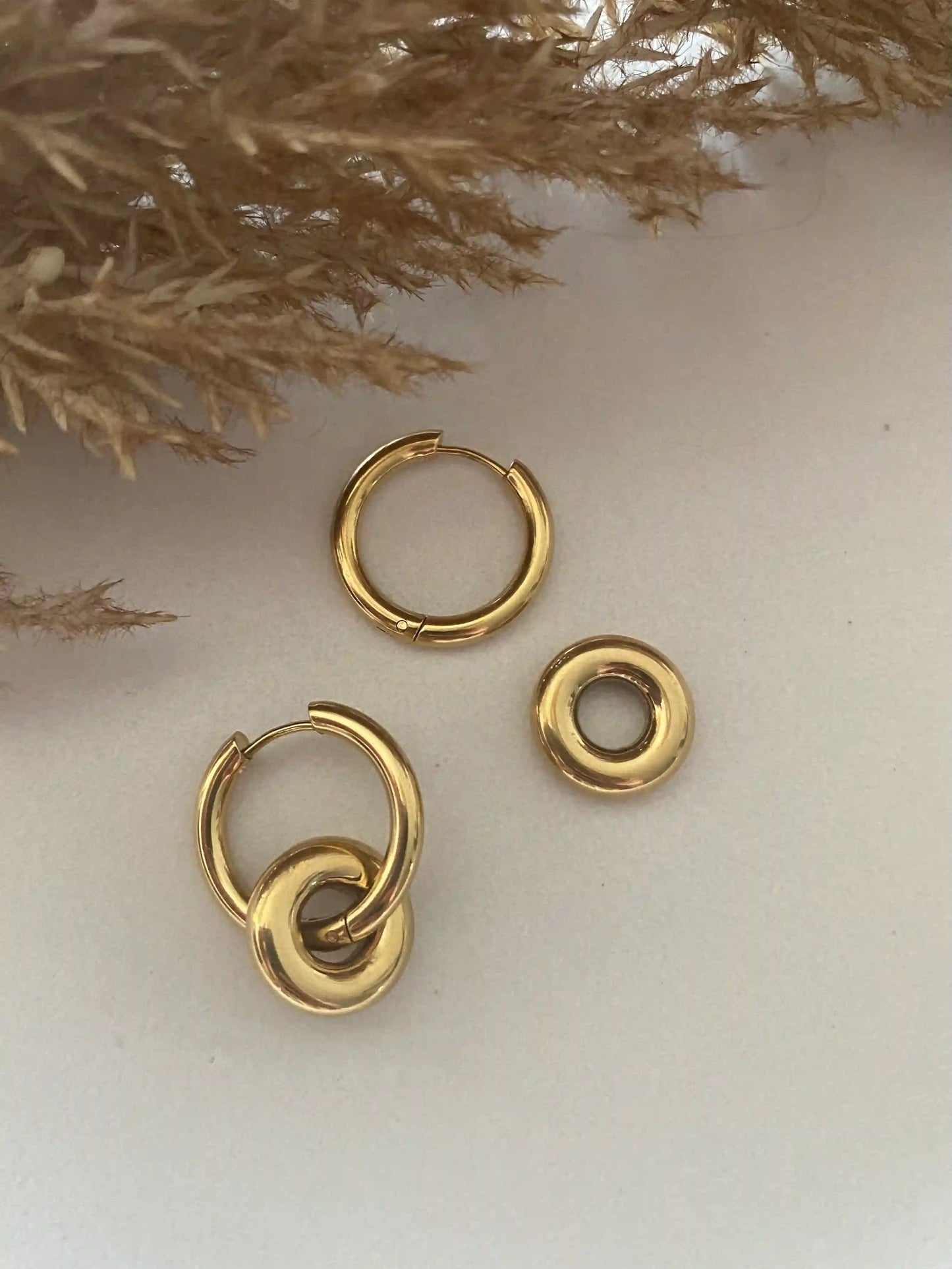 Son aros de acero dorado con diseño liso y cierre de clip. Llevan otro aro entrelazado que es extraible. en acero inoxidable bañado en oro de 18k.
